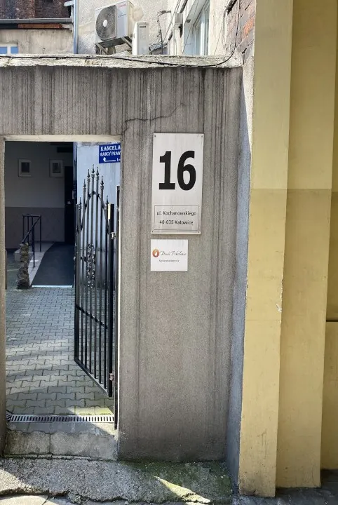 Brama przy numerze 16 przy ulicy Kochanowskiego, obok numeru tabliczka Nowe Pokolenie, za bramą dziedziniec.