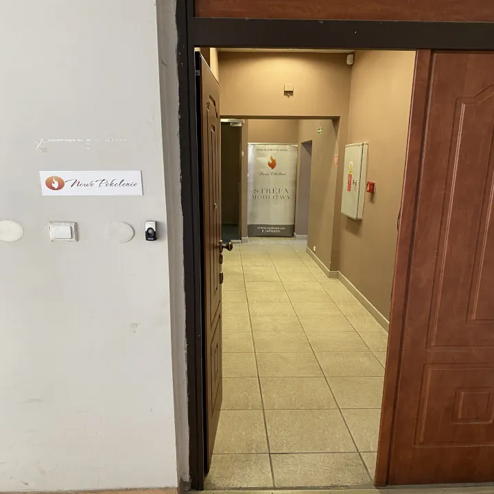 Otwarte drzwi z tabliczką Nowe Pokolenie, za nimi korytarz i baner z napisem Strefa modlitwy.